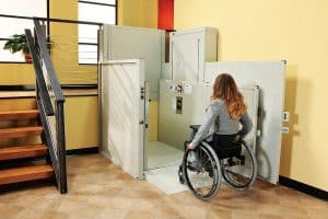 woman in wheelchair using indoor vertical platform lift at bottom of stairs
