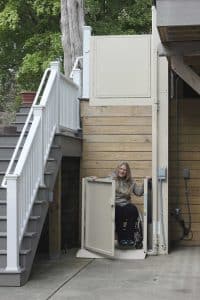 woman in wheelchair using outdoor vertical residential platform lift at bottom