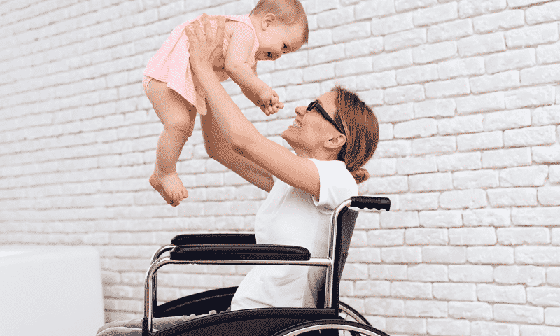 woman in wheelchair holding up baby