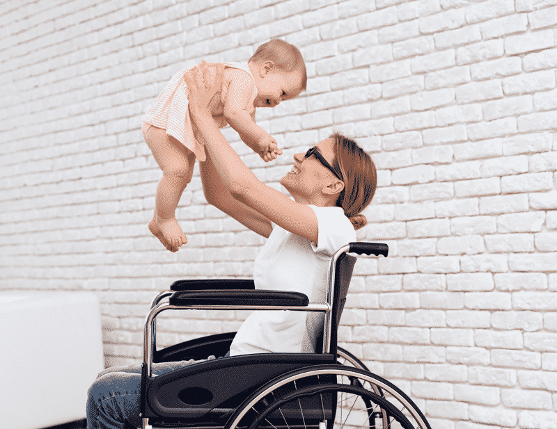 woman in wheelchair holding up baby