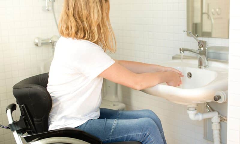 woman in wheelchair washing hand in bathroom