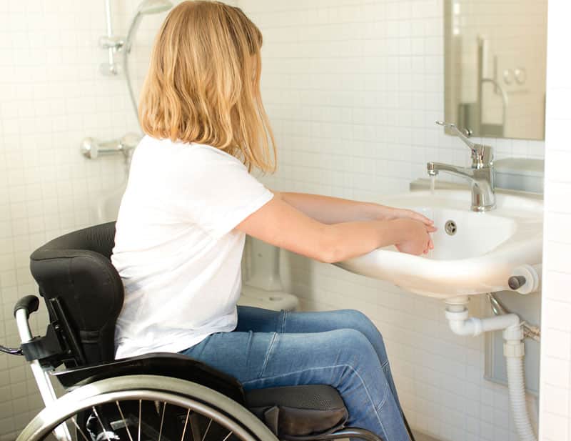 woman in wheelchair washing hand in bathroom