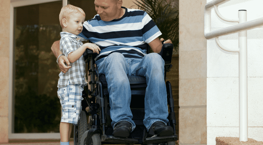 man in wheelchair with arms around stading child