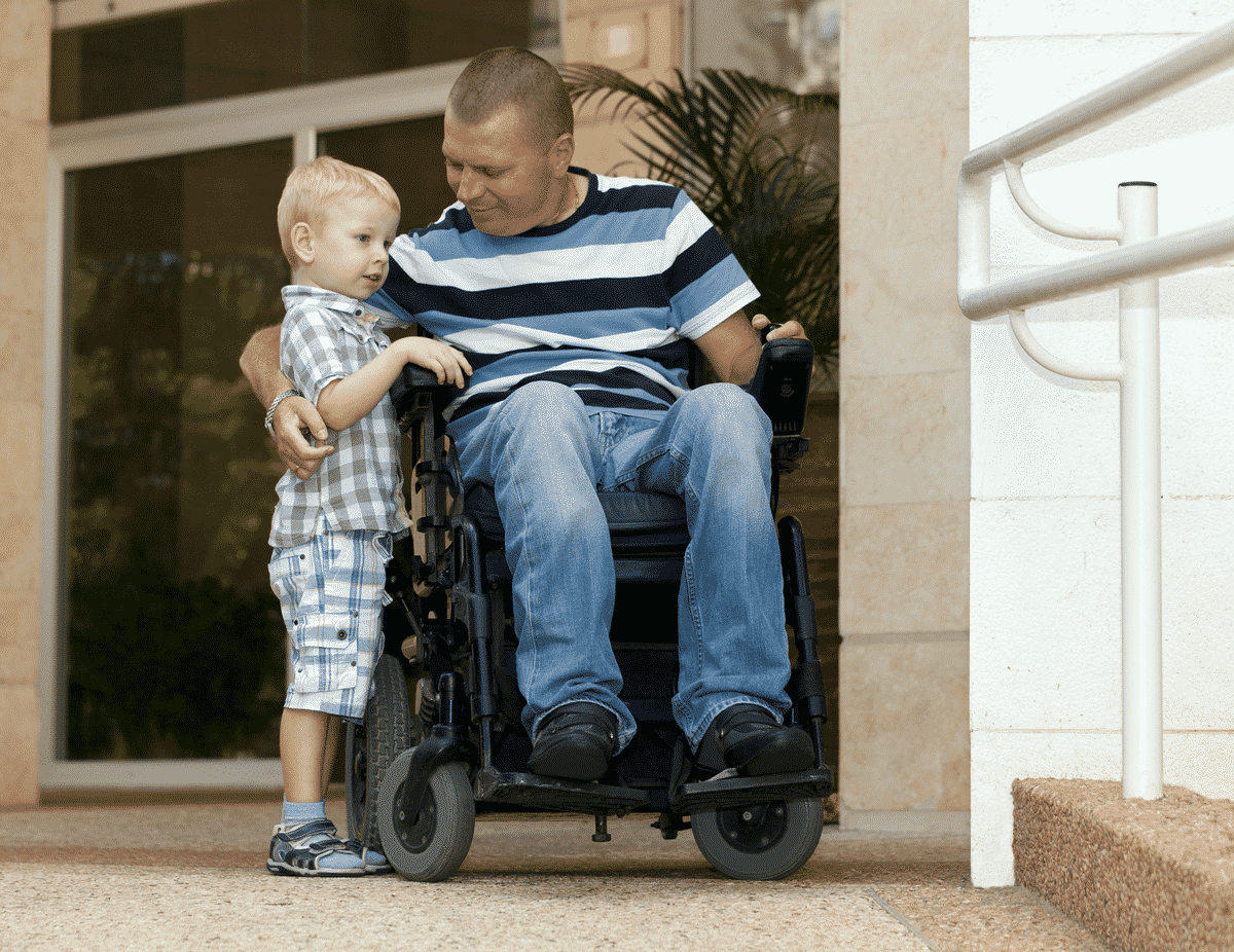 man in wheelchair with arms around stading child